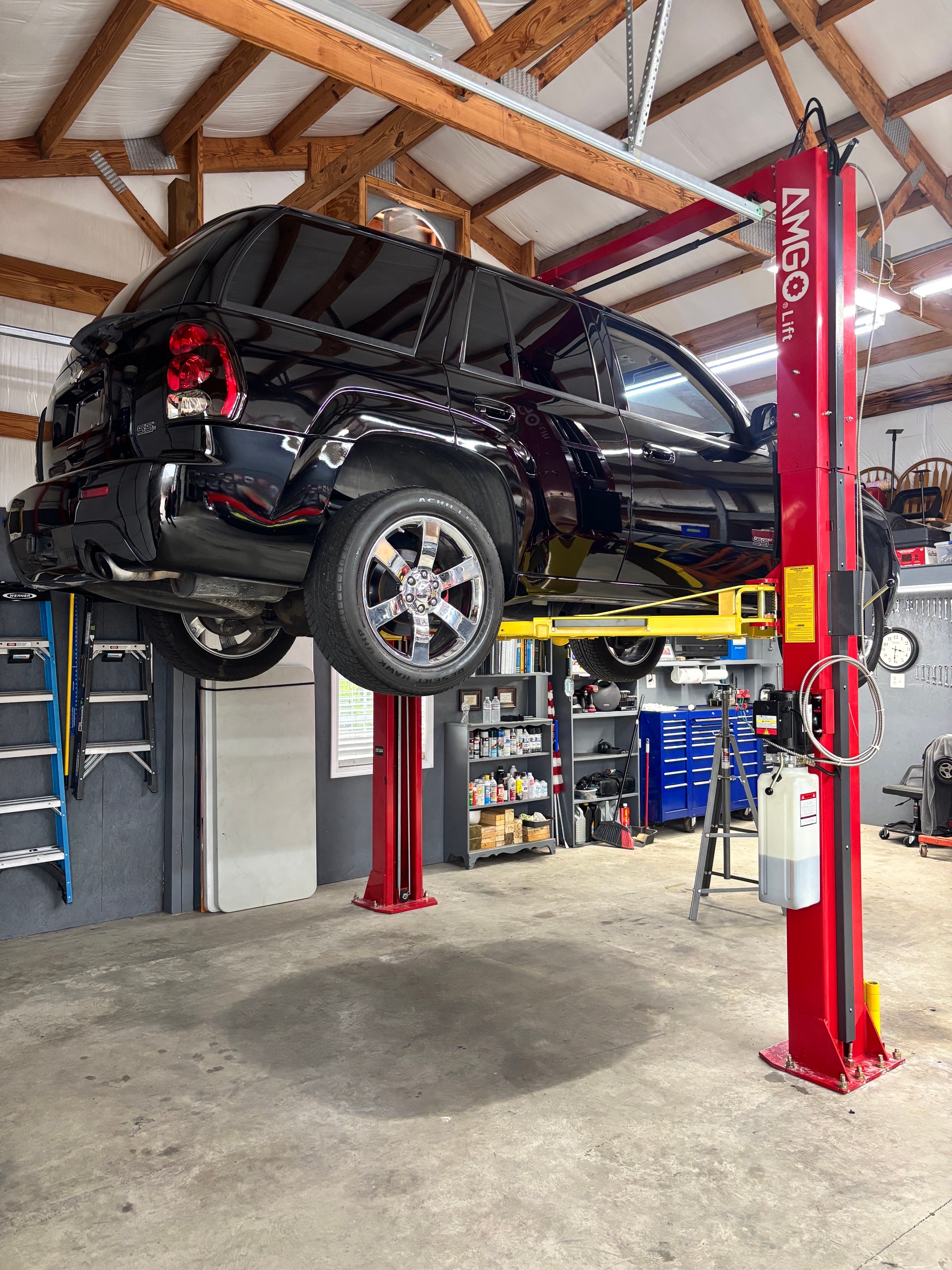 Red AMGO two-post lift with a black SUV raised in a barn-style shop