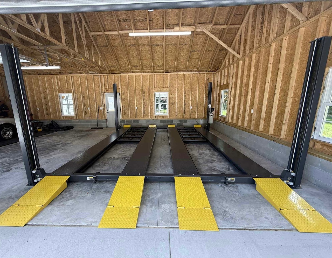 Black 4-post lift with runways down in a new construction garage