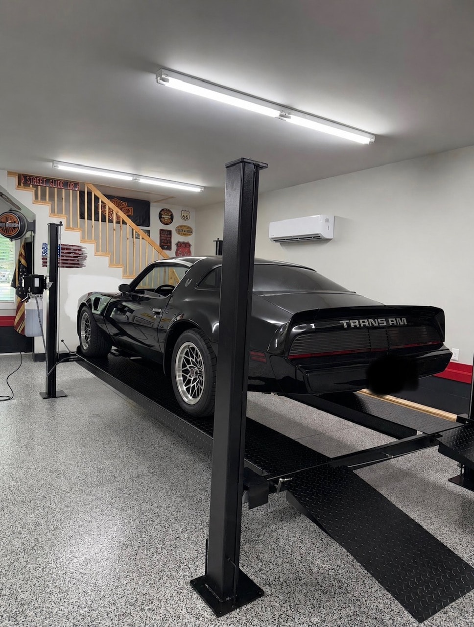Black 4-post lift with a black Pontiac Trans Am in a finished garage