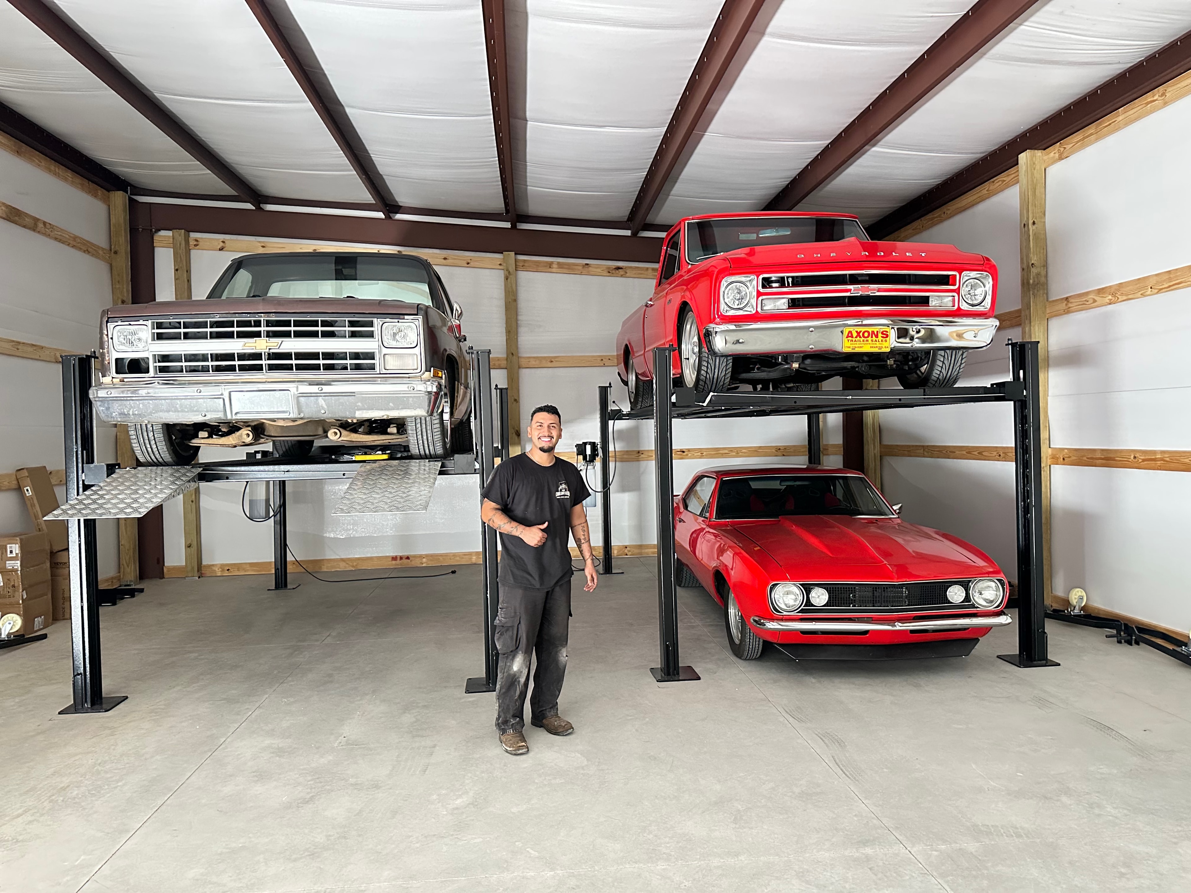 Technician standing in front of two 4-post lifts holding classic Chevrolet trucks and a Camaro